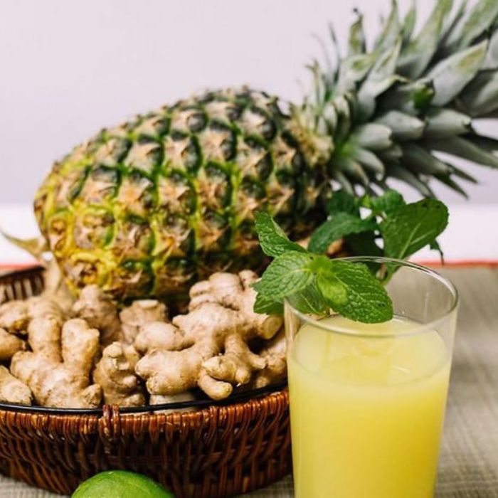 Image of a glass of juice in front of a bowl of filled with limes, ginger and a pineapple.